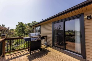 A deck with a grill, a sliding glass door, and a view of a garden. - Lakepoint Overlook | Dock + Lake Access (Bella Vista)