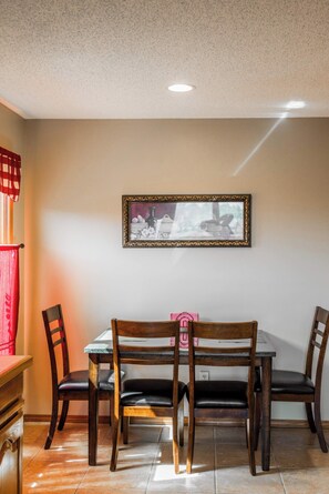 A dining area with a table and four chairs, a framed picture on the wall, and a red curtain on the left. - Lakepoint Overlook | Dock + Lake Access (Bella Vista)