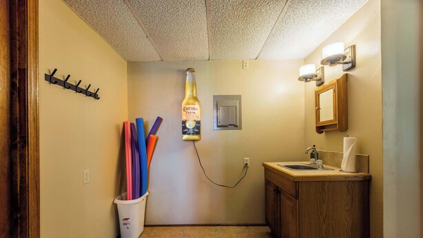 A bathroom with a toilet, sink, and mirror. There is a bottle of Corona Extra beer hanging from the ceiling. - Lakepoint Overlook | Dock + Lake Access (Bella Vista)