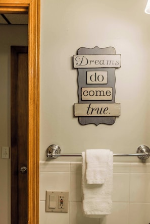 A bathroom with a towel rack, a wall-mounted sign with the phrase 'Dreams do come true.', and a light switch. - Lakepoint Overlook | Dock + Lake Access (Bella Vista)