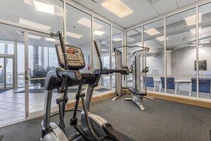 A gym with exercise equipment, large windows, and a view of the city. - Admirals Quarters 1201 (Orange Beach)
