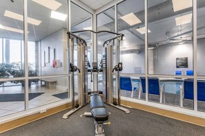 A gym with exercise equipment, a bench, and a view of a pool through large windows. - Admirals Quarters 1201 (Orange Beach)