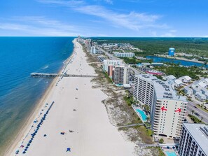 A coastal hotel with a beach view, multiple swimming pools, and a pier extending into the ocean. - Admirals Quarters 1201 (Orange Beach)