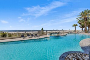 A clear blue pool with lounge chairs and a lifeguard stand, surrounded by a fence and palm trees. - Admirals Quarters 1201 (Orange Beach)