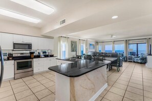 A spacious kitchen with a large island, white cabinetry, and a dining area with a view. - Admirals Quarters 1201 (Orange Beach)