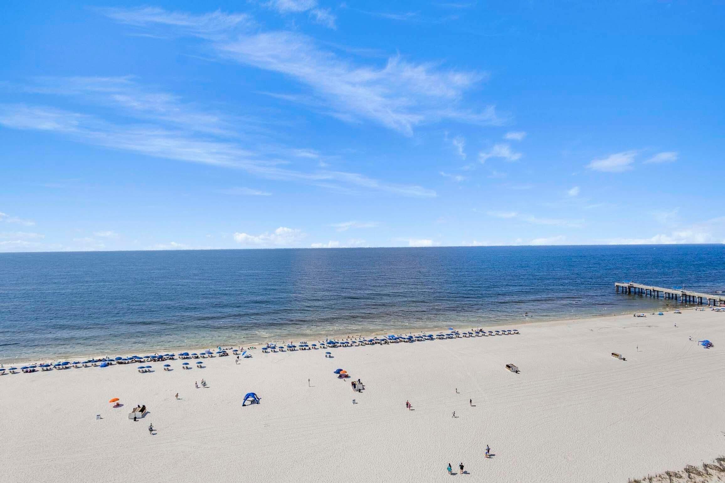 A beach with a pier extending into the water, clear skies, and a sandy shore.