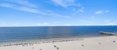 A beach with a pier extending into the water, clear skies, and a sandy shore.