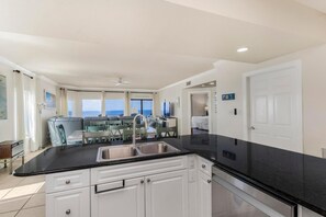 A modern kitchen with a black countertop, white cabinets, and a stainless steel sink. - Admirals Quarters 1201 (Orange Beach)