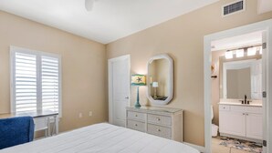 A bedroom with a bed, dresser, mirror, and a bathroom visible through an open door. - Admirals Quarters 1201 (Orange Beach)