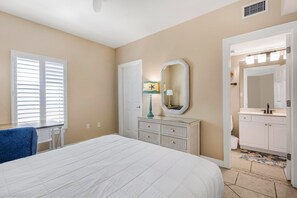 A bedroom with a bed, dresser, mirror, and a bathroom visible through an open door. - Admirals Quarters 1201 (Orange Beach)