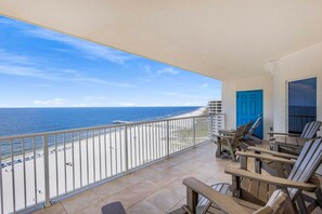 A balcony with a view of the beach and ocean, featuring a blue door, two lounge chairs, and a railing. - Admirals Quarters 1201 (Orange Beach)