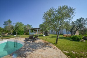 Ein Garten mit Swimmingpool, Liegestühlen, einer Pergola und einem kleinen Gebäude.
