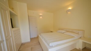 Ein Schlafzimmer mit Bett, Kleiderschrank, Tür und einer Wandleuchte.