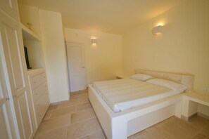 Ein Schlafzimmer mit Bett, Kleiderschrank, Tür und einer Wandleuchte.