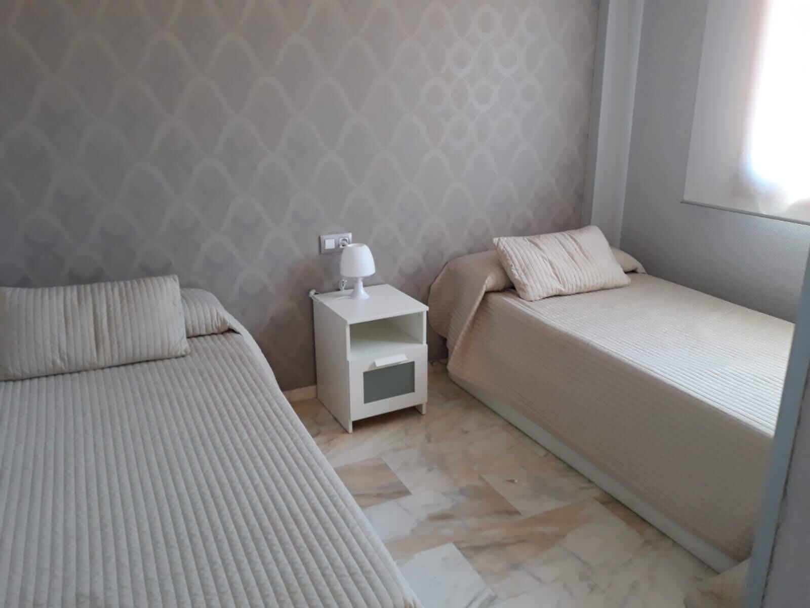 A bedroom with two beds, a nightstand with a lamp, and a patterned wall.