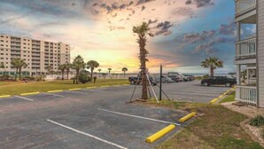 A parking lot with marked spaces, a palm tree, and a building with balconies. - Welcome to Your Beachside Escape Tucked Away on the Serene Fort Morgan Peninsula (Gulf Shores)