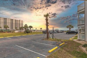 A parking lot with marked spaces, a palm tree, and a building with balconies. - Welcome to Your Beachside Escape Tucked Away on the Serene Fort Morgan Peninsula (Gulf Shores)