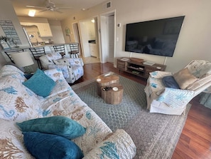 A living room with a sofa, chairs, a coffee table, a TV, and a kitchen in the background. - Welcome to Your Beachside Escape Tucked Away on the Serene Fort Morgan Peninsula (Gulf Shores)
