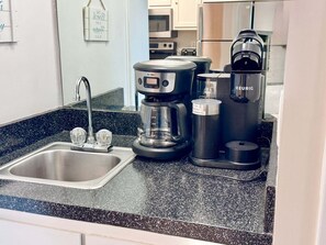 A kitchen with a stainless steel sink, a coffee maker, a Keurig coffee maker, and a water dispenser. - Welcome to Your Beachside Escape Tucked Away on the Serene Fort Morgan Peninsula (Gulf Shores)