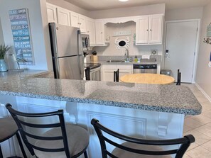 A kitchen with white cabinets, a granite countertop, a stainless steel refrigerator, and a sink. - Welcome to Your Beachside Escape Tucked Away on the Serene Fort Morgan Peninsula (Gulf Shores)