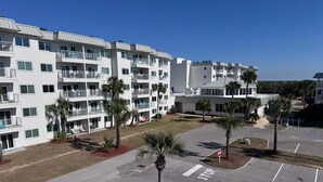 A multi-story hotel with balconies, a parking lot, and palm trees. - Welcome to Your Beachside Escape Tucked Away on the Serene Fort Morgan Peninsula (Gulf Shores)