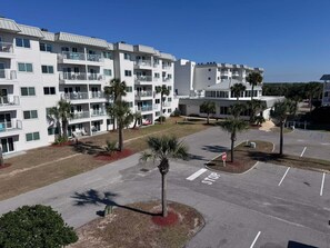 A multi-story hotel with balconies, a parking lot, and palm trees. - Welcome to Your Beachside Escape Tucked Away on the Serene Fort Morgan Peninsula (Gulf Shores)