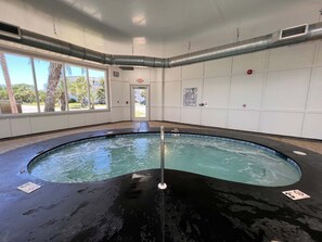Une piscine intérieure avec de grandes fenêtres offrant une vue dégagée sur l’extérieur, un panneau de signalisation indiquant clairement la sortie, et un espace au bord de la piscine comprenant un poste de surveillance pour les sauveteurs.