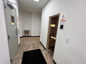 A hotel corridor with a sauna sign, a trash bin, and a door leading to a room. - Welcome to Your Beachside Escape Tucked Away on the Serene Fort Morgan Peninsula (Gulf Shores)