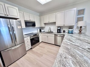 A modern kitchen with white cabinets, stainless steel appliances, a marble countertop, and a skylight. - Marlin Key 2B Your Gulf-front Escape in Beautiful Orange Beach, Alabama (Orange Beach)