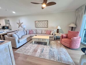 A living room with a sectional sofa, a coffee table, a red armchair, a star decoration, a lamp, and a ceiling fan. - Marlin Key 2B Your Gulf-front Escape in Beautiful Orange Beach, Alabama (Orange Beach)