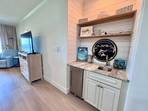 A kitchen with a built-in dishwasher, a sink, and a countertop. There is a television in the adjacent living area. - Marlin Key 2B Your Gulf-front Escape in Beautiful Orange Beach, Alabama (Orange Beach)