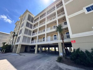 Um hotel com vários andares, varandas, área de estacionamento coberta e um sinal de ligação para o corpo de bombeiros.