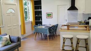 Een compacte woonruimte met een eethoek, een bank, een keuken met fornuis en een raam met gordijnen.