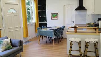 A compact living space with a dining area, a sofa, a kitchen with a stove, and a window with curtains.