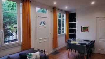 A room with a dining table, chairs, a sofa, and large windows with curtains.