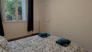 Een slaapkamer met een bedovertrek met een patroon, een radiator, een witte deur en een raam met gordijnen.