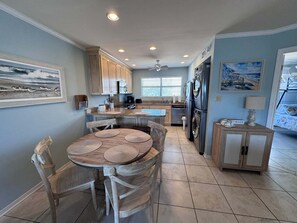 A kitchen with a dining area, wooden cabinets, a refrigerator, and a window with blinds. - Coastal Comfort w/ Pool + Easy Beach Access 2br/2ba (Orange Beach)