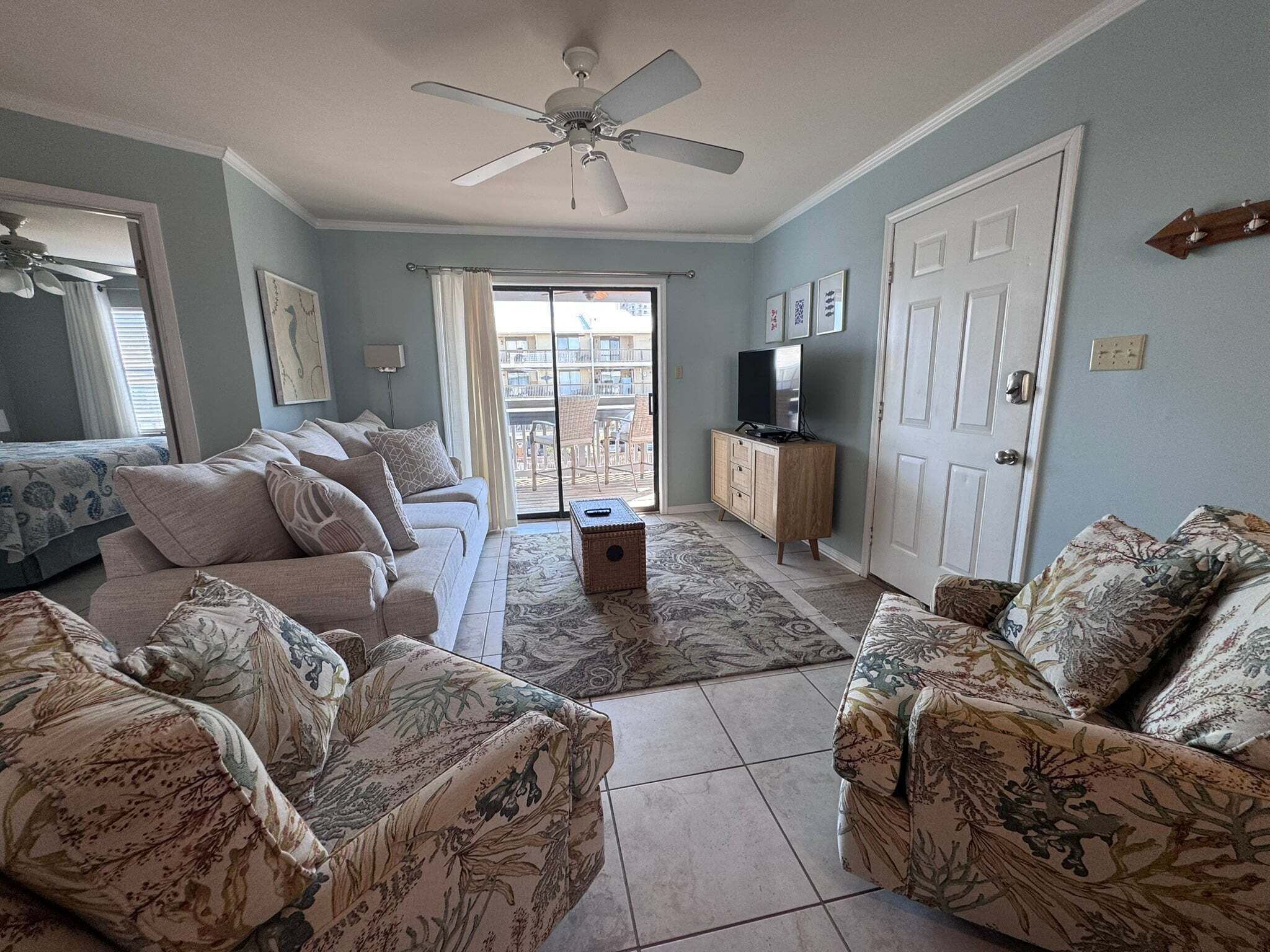 A living room with a ceiling fan, a television, a sofa set, and a sliding glass door leading to an outdoor area.