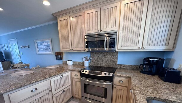 A kitchen with wooden cabinets, a stainless steel stove, a microwave, and a coffee maker. - Coastal Comfort w/ Pool + Easy Beach Access 2br/2ba (Orange Beach)
