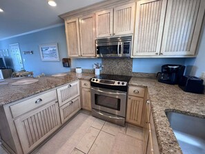 A kitchen with wooden cabinets, a stainless steel stove, a microwave, and a coffee maker. - Coastal Comfort w/ Pool + Easy Beach Access 2br/2ba (Orange Beach)
