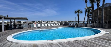 Une terrasse en bois avec une piscine, des chaises longues et des palmiers.