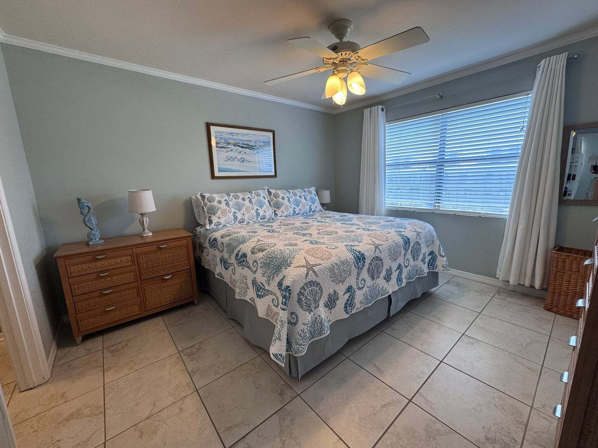 A bedroom with a bed, a nightstand, a ceiling fan, a window with blinds, and a framed picture on the wall.