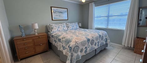 A bedroom with a bed, a nightstand, a ceiling fan, a window with blinds, and a framed picture on the wall.