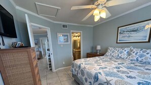 A bedroom with a bed, a ceiling fan, a painting, and a door leading to a bathroom. - Coastal Comfort w/ Pool + Easy Beach Access 2br/2ba (Orange Beach)