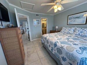 Ein Schlafzimmer mit einem Bett, einem Deckenventilator, einem Gemälde und einer Tür zu einem Badezimmer.