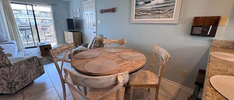 A dining area with a round wooden table and chairs, a ceiling fan, and a view of the outside balcony.