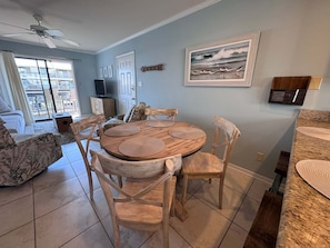 A dining area with a round wooden table and chairs, a ceiling fan, and a view of the outside balcony. - Coastal Comfort w/ Pool + Easy Beach Access 2br/2ba (Orange Beach)