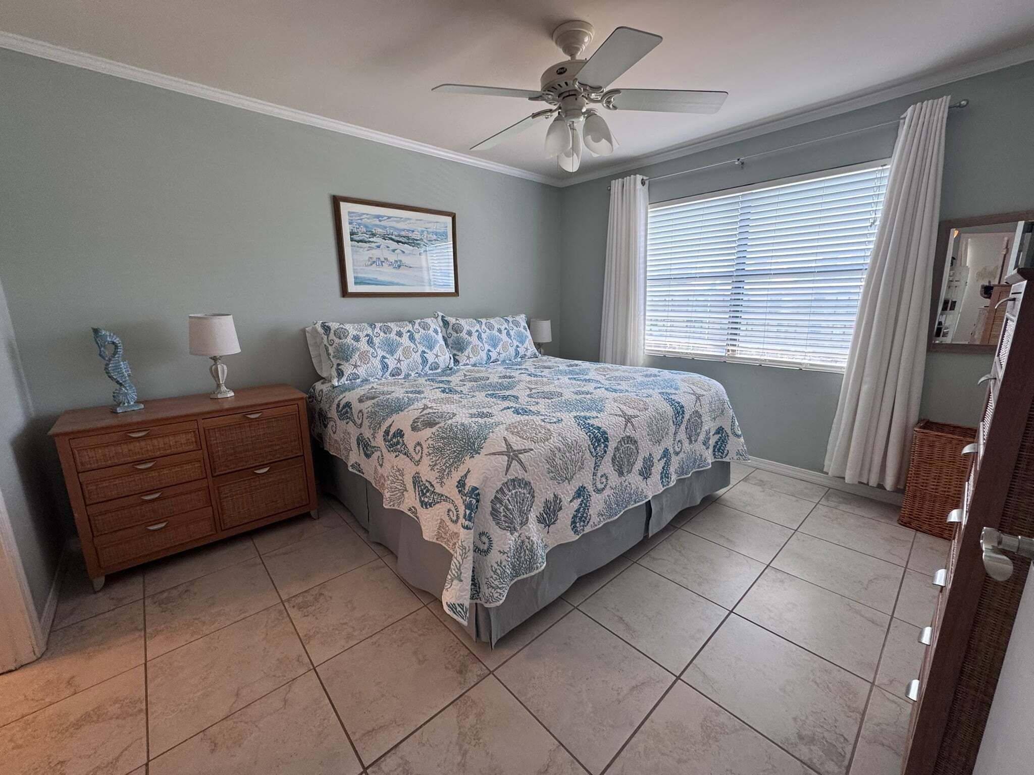 A bedroom with a bed, nightstand, dresser, ceiling fan, window with blinds, and a framed picture on the wall.
