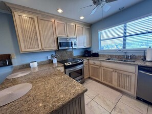 A kitchen with granite countertops, stainless steel appliances, wooden cabinets, and a window with blinds. - Coastal Comfort w/ Pool + Easy Beach Access 2br/2ba (Orange Beach)
