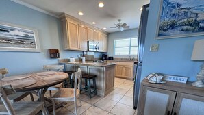 A kitchen with wooden cabinets, a dining table with chairs, a refrigerator, and a ceiling fan. - Coastal Comfort w/ Pool + Easy Beach Access 2br/2ba (Orange Beach)